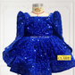 A royal blue sequined children's dress by house of claire displayed on a mannequin against a white decorative wall. The dress has a square neckline, puffed sleeves, and a tiered ruffled skirt. www.houseofclaire.com