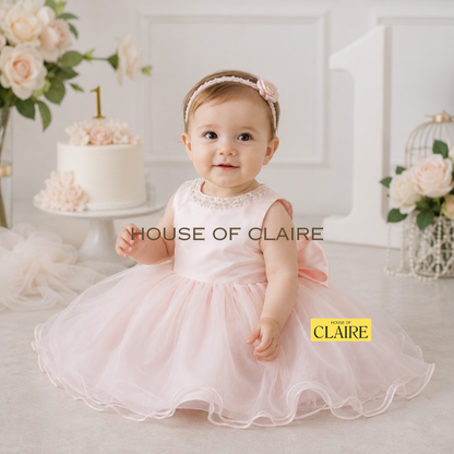 Luxury blush pink 1st birthday dress for baby girls featuring a satin bodice, layered organza skirt, and oversized bow by House of Claire